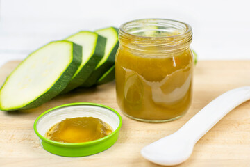 Baby food. A glass jar with children's mashed green zucchini puree and a lid on a wooden background. The first lure of the baby.