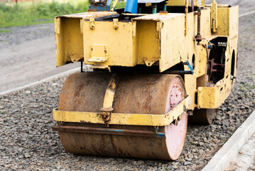 Mini road roller leveling a soil with gravel substructure for a new walkway in an urban settlement. The road construction. Rural driveway