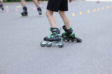 A child rides black and green roller skates. Cropped shot of a little boy learning to rollerblade on asphalt.