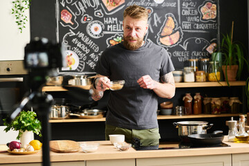 Modern male food blogger with beard on face holding glass bowl with fried sesame seeds speaking...