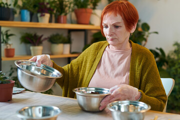 Red haired mature woman transplanting seedlings in bigger bowls at table