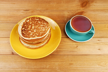 Homemade pancakes in a yellow plate and a cup of tea on a wooden table