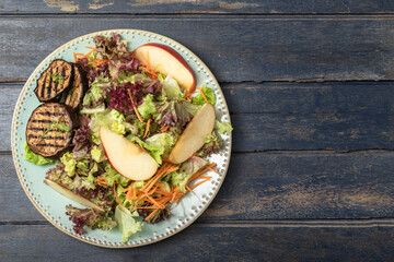 Healthy food apple salad with roasted eggplant red lettuce in plate has fork on blue wood table.