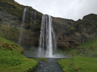 A foss waterfall in iceland with a grey sky and green grass around the river water flow on a roadtrip brak stop vacation