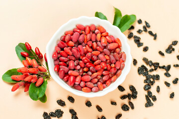Fresh red and dried barberry berries with green leaves on a beige background. Close-up, top view.