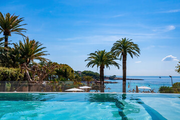 Fototapeta na wymiar Swimming pool with view of trees and seascape. Scenic view of ocean against blue sky. Hotel spa on Mediterranean seaside during summer.