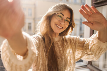 Happy caucasian adult blond woman waving at camera smiling with teeth on sunlight background....