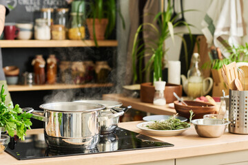 Horizontal shot of saucepans or pots with hot boiling water on modern electric cooker in loft kitchen