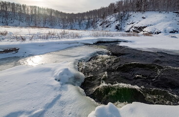 Winter landscape with birch trees on the mountain shore, snow and flowing river water