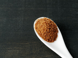 Spoon of coconut brown sugar on dark wooden background. Top view of full white ceramic spoon with raw organic coconut sugar from crystallized sap of cut flower buds coconut palm. Copy space. Closeup