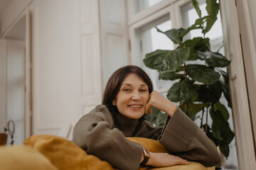 Close-up of funny middle-aged lady spending time on sofa in living room of her apartment. Brunette...