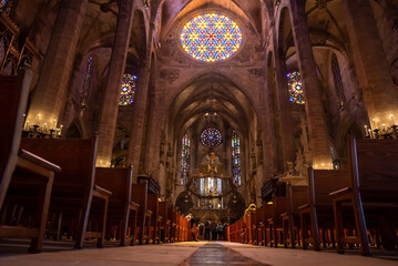 Mallorca, Spain. April 27, 2022. Low angle view of stained glass ceiling and pews in medieval La Seu Cathedral. Tourists praying at beautiful gothic church. Interior of historic religious place. © Aerial Film Studio