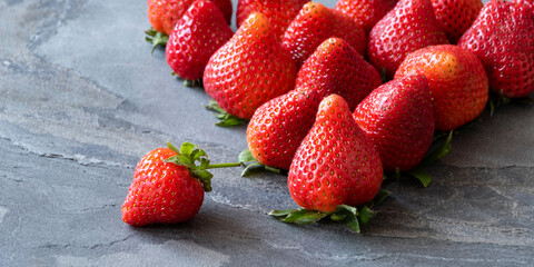 Fresh ripe red strawberries with green calyx leaves on grey stone texture background. One strawberry stands out of others