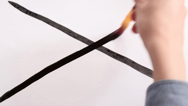 Drawing on white paper crosshairs with a brush in black ink.