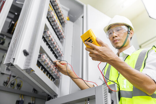 Electrical engineer or repairman holding digital multimeter to inspecting the electrical system in a factory.