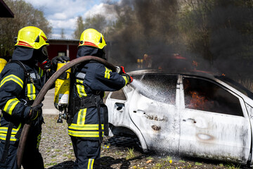 Obraz premium Feuerwehrmänner löschen ein brennendes Auto