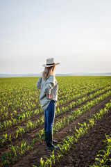 Proud satisfied farmer is looking at corn field in cultivated land. Woman with straw hat standing...