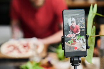 Selective close-up shot of Caucasian food blogger filming delicious pizza cooking process on smartphone camera