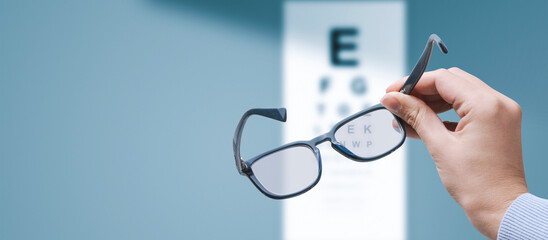 Optometrist holding glasses and eye chart - obrazy, fototapety, plakaty