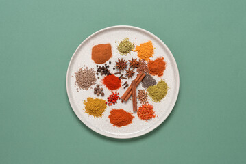 Various spices on a plate, green pastel background. Top view, flat lay.