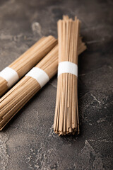 Buckwheat paste on a black cement background. Raw noodles. Ingredients for a gluten-free dish. Dried buckwheat soba noodles. Traditional Japanese food. Healthy food. Place to copy.
