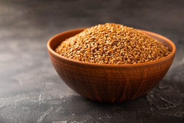Buckwheat in a bowl on a black textured marble background. Raw buckwheat. Ingredients for gluten free cereal. Healthy food. Place to copy.