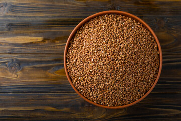 Buckwheat in a bowl on a brown wooden background. Raw buckwheat. Ingredients for gluten-free porridge.Healthy food. Place to copy.