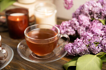 A cup of green tea against the background of a spring bouquet of lilacs . Romantic composition with books and candles. spring tea drink. Place to copy. Romantic concept.