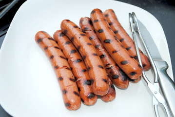 Cooked Hotdogs on a White Plate with Tongs and a Knife