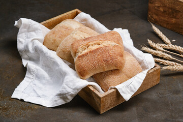 Italian ciabatta bread or bun in a wooden box with white kitchen towel. Freshly baked traditional bread. Homemade rustic atisan bread or Italian Ciabatta. Shallow depth of field
