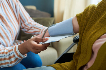 Close-up of nurse checking blood pressure of senior patient during visit to home