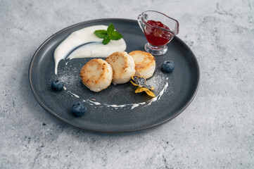 Cottage cheese pancakes, syrniki on plate with sour cream and jam, blueberry and edible flowers. Healthy and delicious morning breakfast.