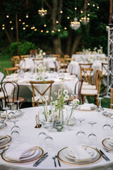 magical rustic wedding tables outside in the garden with hanging light and flowers, chairs, outdoor ceremony in the open air
