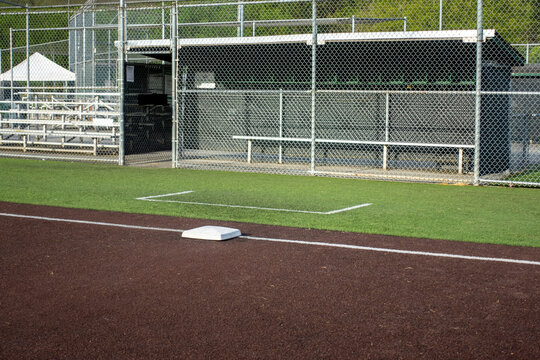 Angled view of a white base on a baseball field, with the view of a dugout in the background