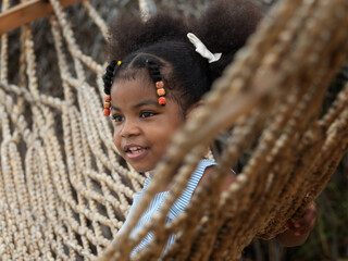 Portrait of cute African girl sitting on thread hammock. Close up image of Afro girl with colorful beads on the hair in front.