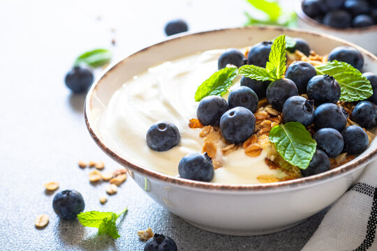 Greek Yogurt with granola and fresh bluebery at light stone table. Close up image.
