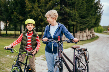 Grandmother and grandson on bikes outdoors smiling and talking. Different generation family communication concept.