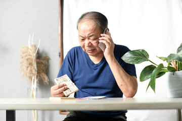 札束を持ちながら電話をする高齢者男性