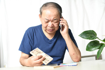 札束を持ちながら電話をする高齢者男性
