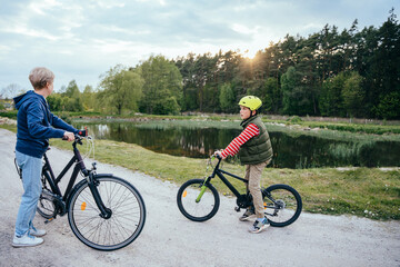 Active senior grandmother and child boy riding bikes in nature with lake on background.