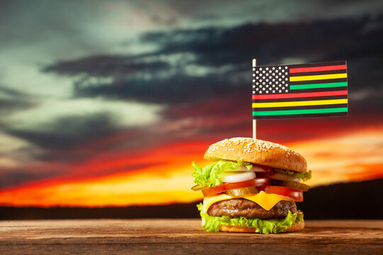 Classic American burger with alternative African American juneteenth flag on the top over sunset background. Close-up with selective focus.