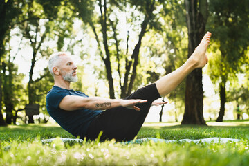 Mature handsome man in sporty clothes doing workout practicing yoga fitness outdoors outside in...