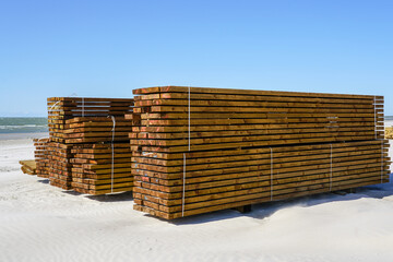 Large stacks of impregnated brown pine wood boards by the sea on a sandy beach