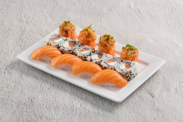 Fresh made sushi mix. Different kinks of salmon sushi served on white plate. Studio shoot on slated background.