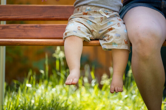 Baby grow up concept: Close up of barefoot baby feet sitting on park bench, summer time