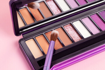 Colorful eye shadow palette on pink background. Color eyeshadow palette with brush for day and...