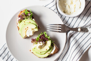 Two sandwiches with avocado and lettuce on a plate are on the kitchen table. The theme of  healthy food. View from the top point.