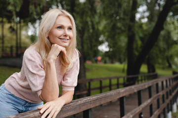 Dreamy pensive caucasian mature blonde woman walking relaxing resting in city park forest spending free time in woods - obrazy, fototapety, plakaty