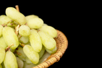 One bunch of white seedless grapes on a ceramic dish, close-up, isolated on a black background.