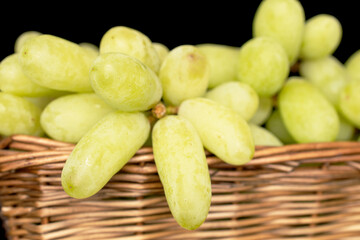 One bunch of white seedless grapes in a basket, close-up, isolated on a black background.